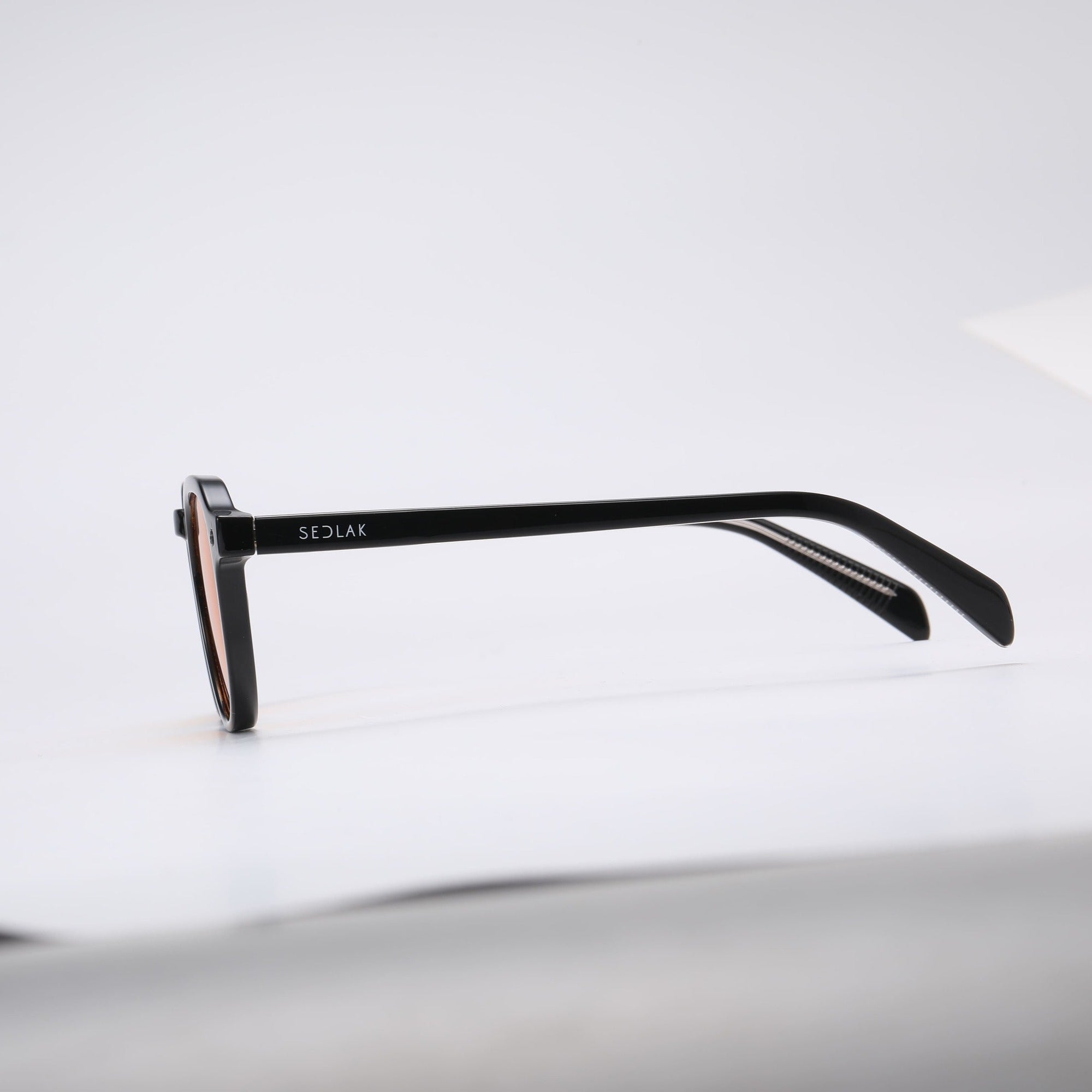 Black square-framed sunglasses with orange lenses on a white background.