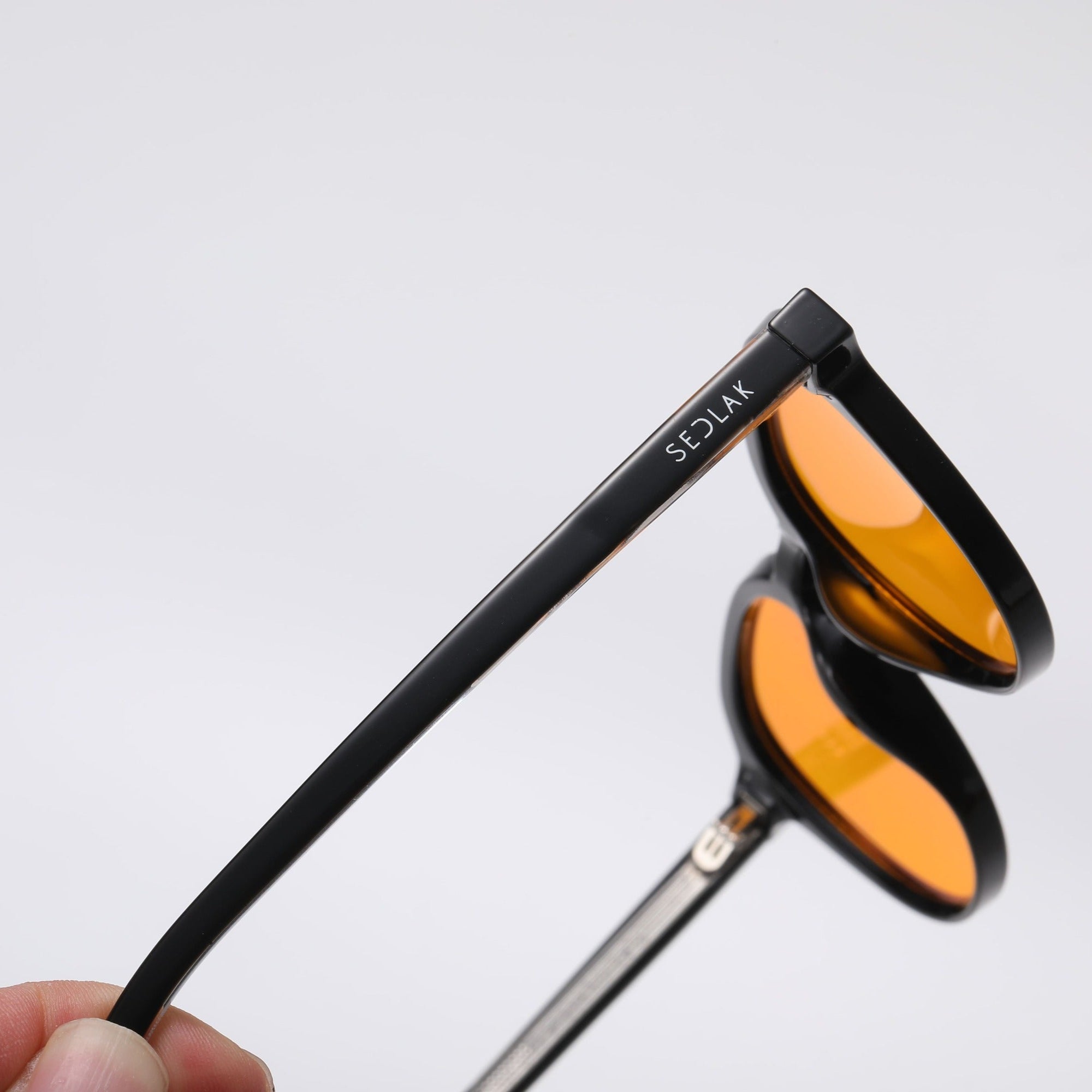 Black square-framed sunglasses with orange lenses on a white background.