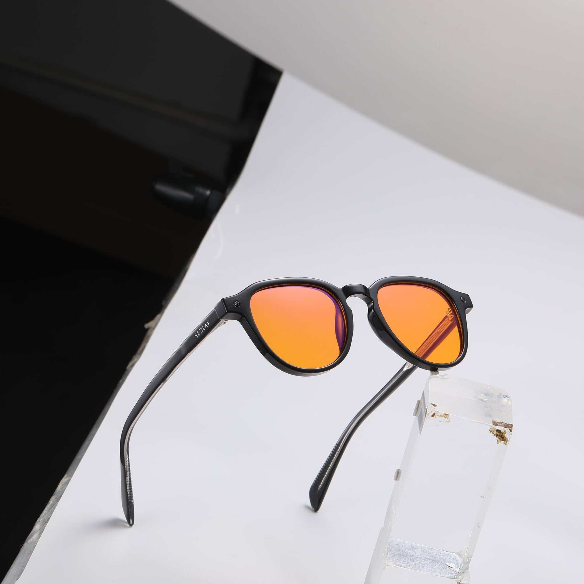 Black square-framed sunglasses with orange lenses on a white background.